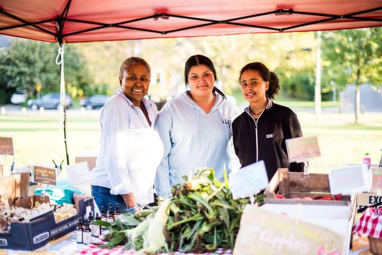 Three neighbors behind a produce stand at the GNA farmers-market booth